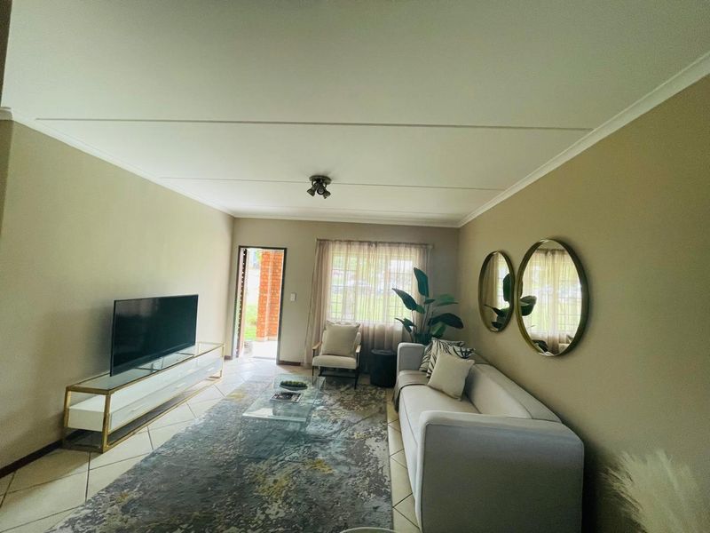 A well-maintained living room featuring tiled flooring, neutral wall tones, and direct access to an outdoor area through a glass-paneled door.