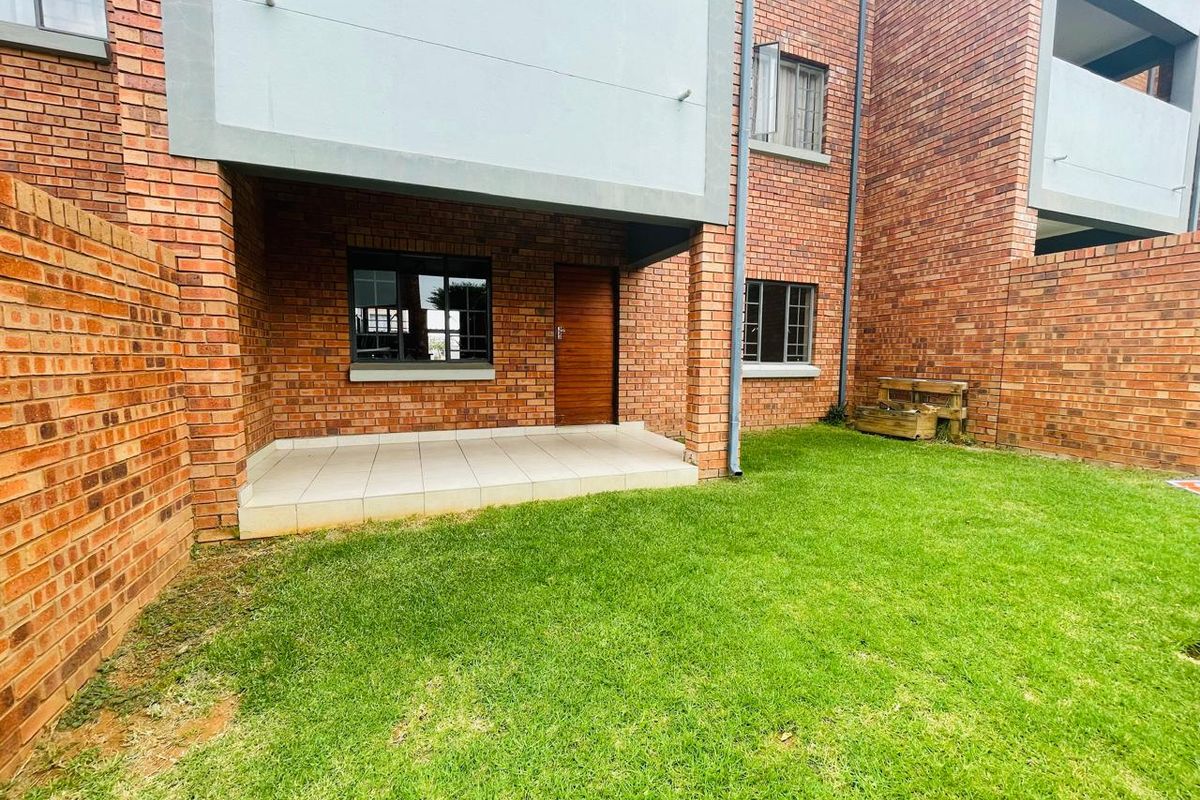 A private rear garden area featuring a paved patio, brick exterior walls, and a well-maintained lawn, providing a functional outdoor space.