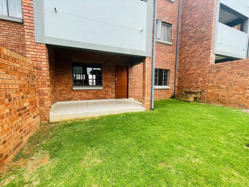 A private rear garden area featuring a paved patio, brick exterior walls, and a well-maintained lawn, providing a functional outdoor space.