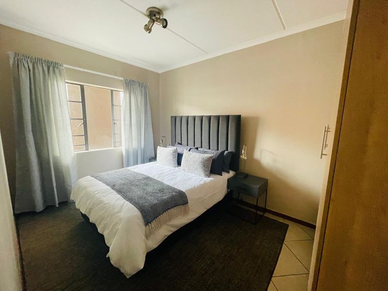 A well-lit bedroom featuring tiled flooring, a built-in cupboard, and a steel-framed window, providing a functional and comfortable living space.