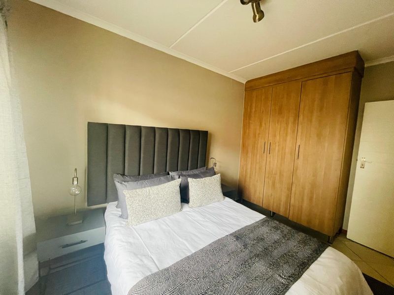A functional bedroom featuring a built-in wooden wardrobe and tiled flooring, providing practical storage and a neutral living space.
