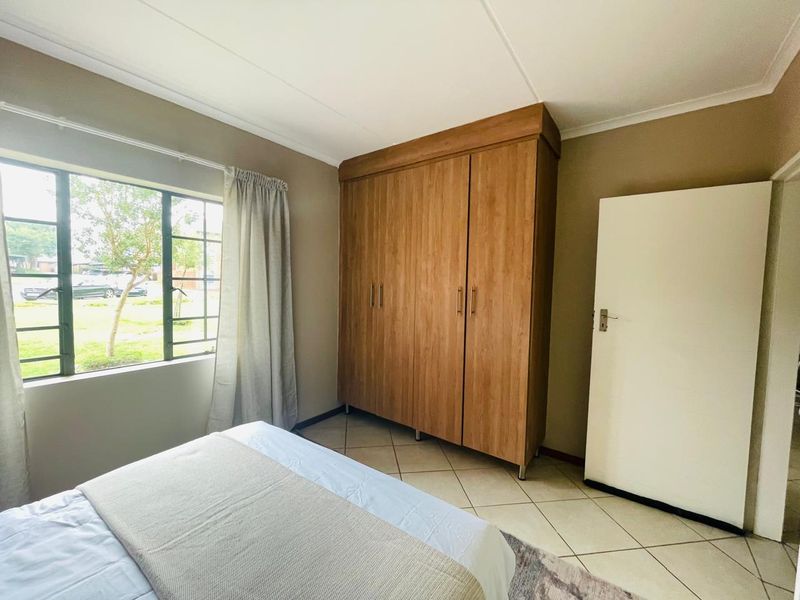 A bedroom featuring tiled flooring, a large built-in wooden wardrobe, and a window with security bars overlooking the exterior.