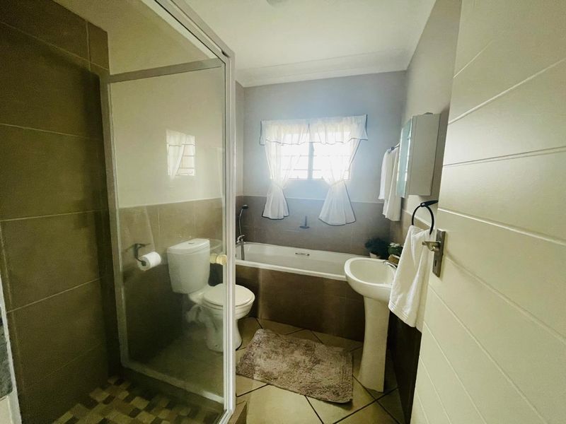 A functional bathroom featuring a shower enclosure, bathtub, pedestal basin, and toilet with neutral wall and floor tiling.