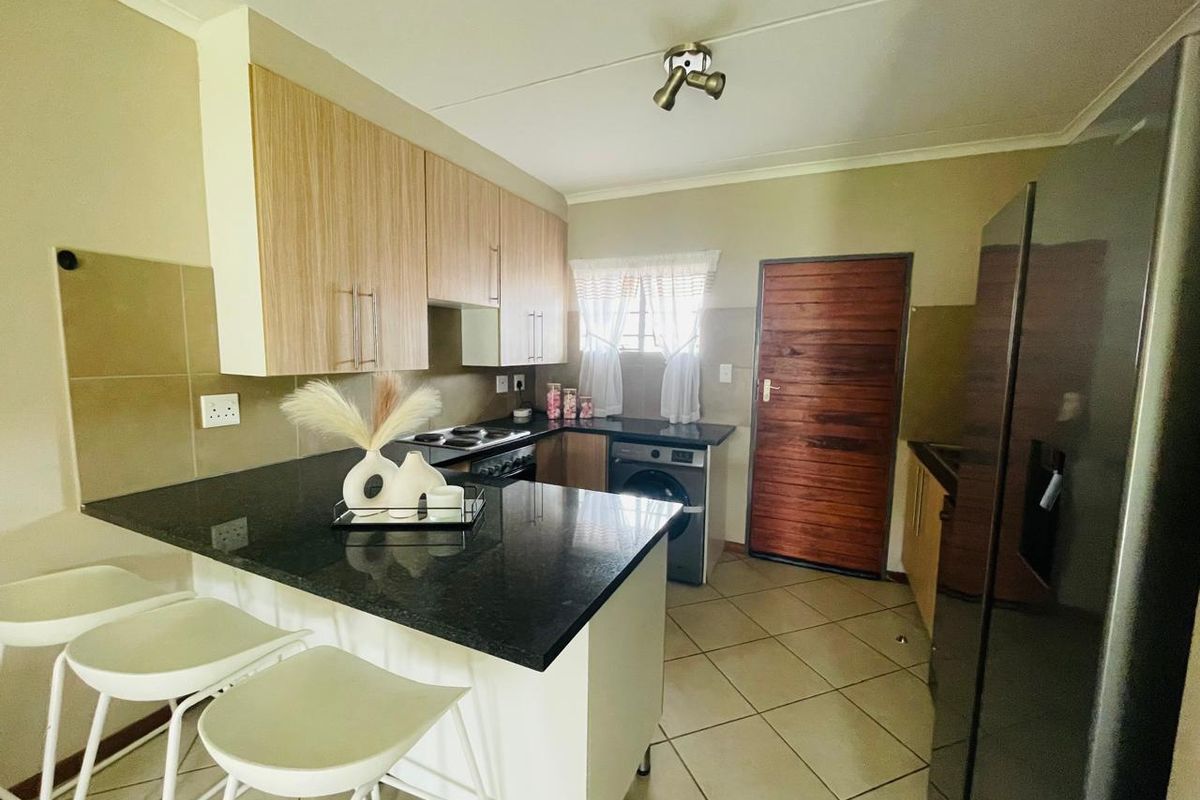 A functional kitchen featuring granite countertops, light wood cabinetry, built-in oven and hob, and tiled flooring with direct access to an exterior door.