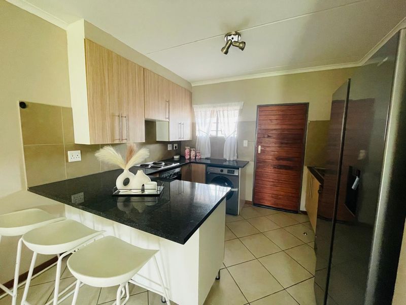 A functional kitchen featuring granite countertops, light wood cabinetry, built-in oven and hob, and tiled flooring with direct access to an exterior door.