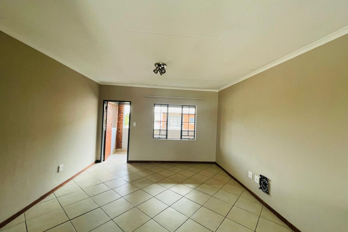 An empty, neutrally painted living room featuring tiled flooring, a ceiling light, and direct access to an outdoor balcony area.