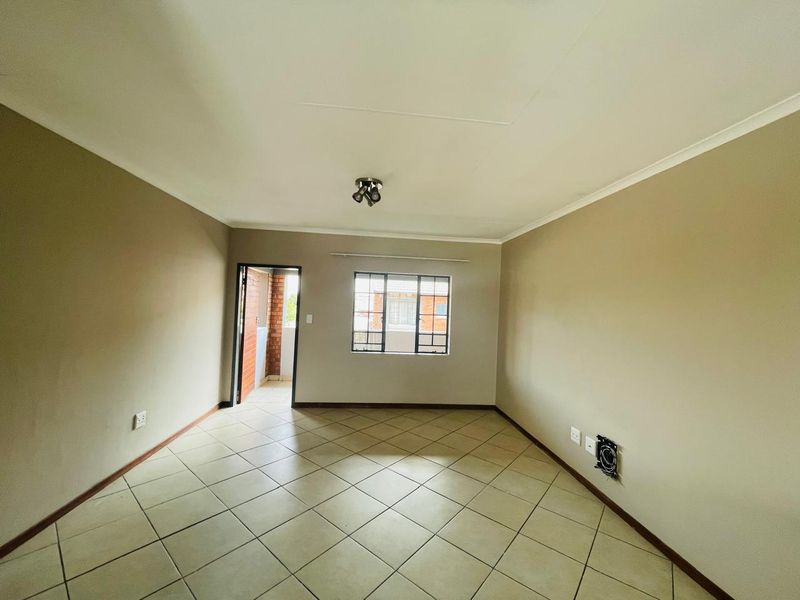 An empty, neutrally painted living room featuring tiled flooring, a ceiling light, and direct access to an outdoor balcony area.