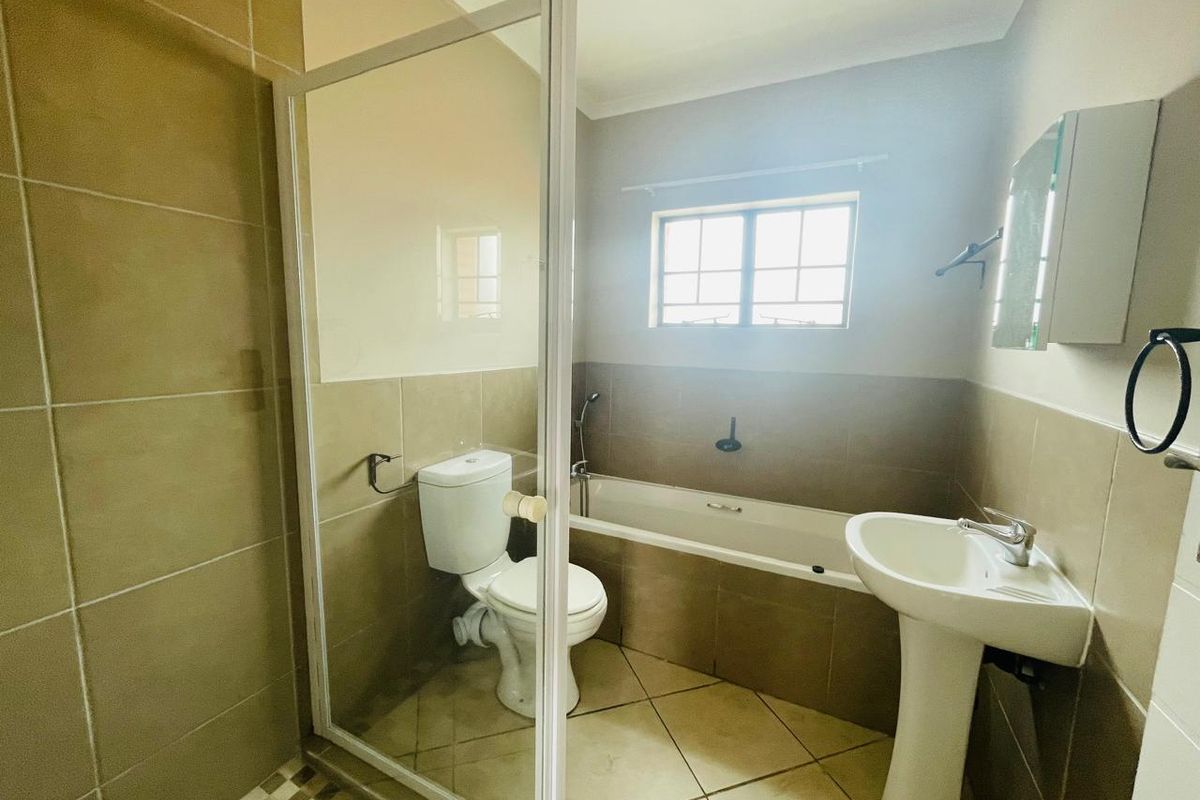 A functional bathroom featuring a pedestal basin, toilet, bathtub, and a separate shower enclosure with neutral wall and floor tiling.
