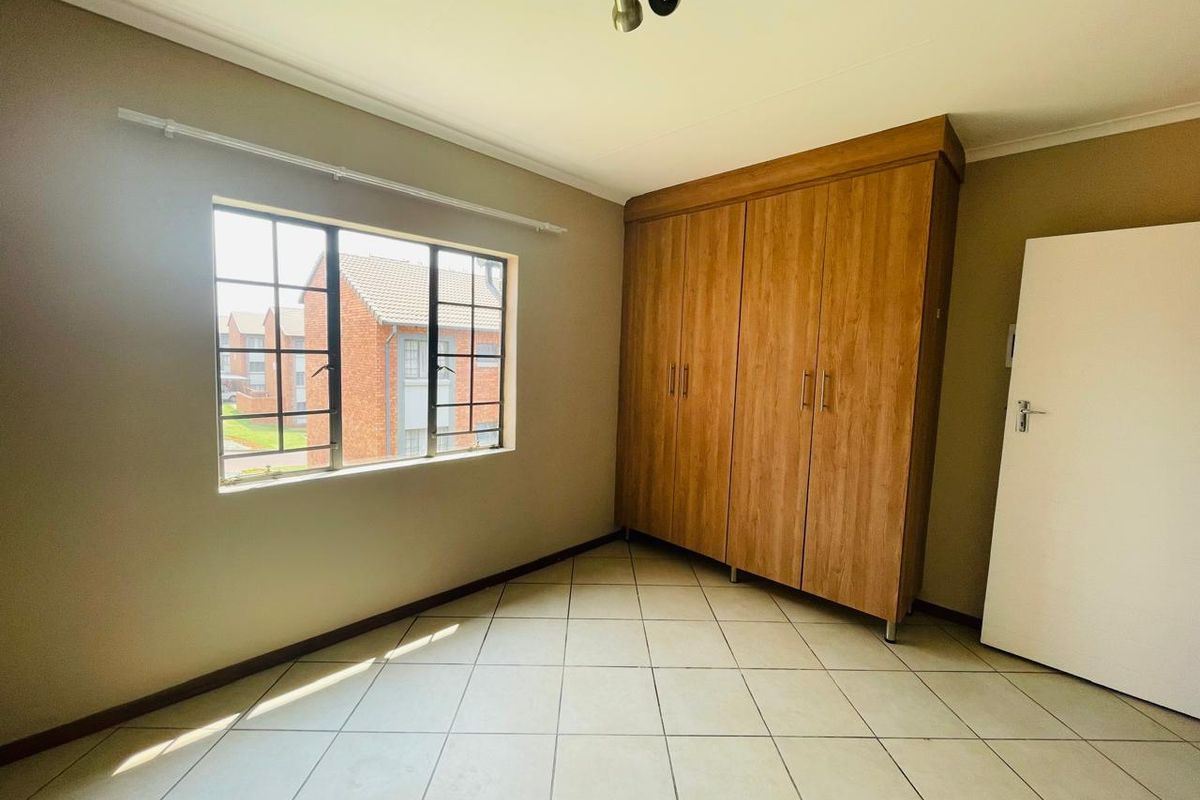 A bright, empty bedroom featuring tiled flooring, neutral walls, and built-in wooden cupboards, offering a clean and functional space.