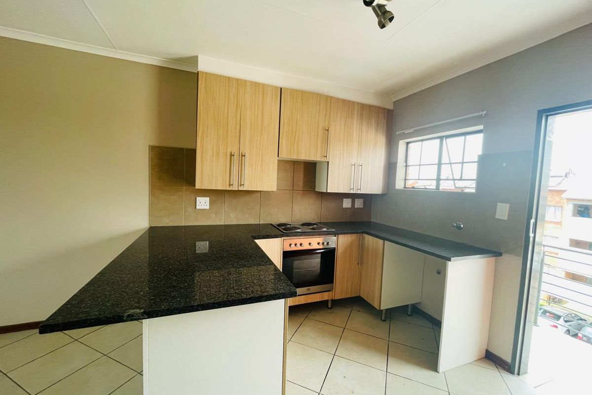 A clean, functional kitchen featuring granite countertops, light wood-finish cabinetry, built-in oven and hob, and tiled flooring with direct access to an outdoor area.