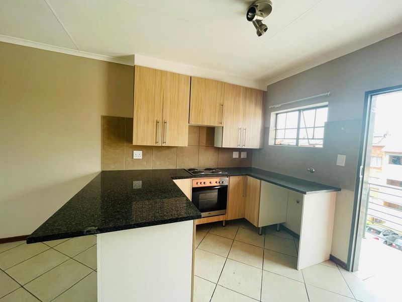 A clean, functional kitchen featuring granite countertops, light wood-finish cabinetry, built-in oven and hob, and tiled flooring with direct access to an outdoor area.
