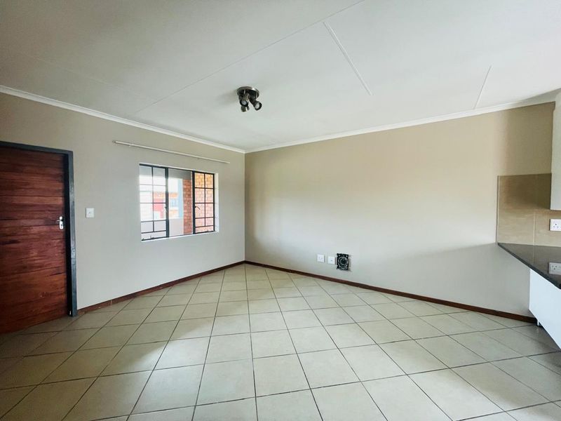 An empty open-plan living and kitchen area featuring tiled flooring, neutral walls, and a window with security bars.