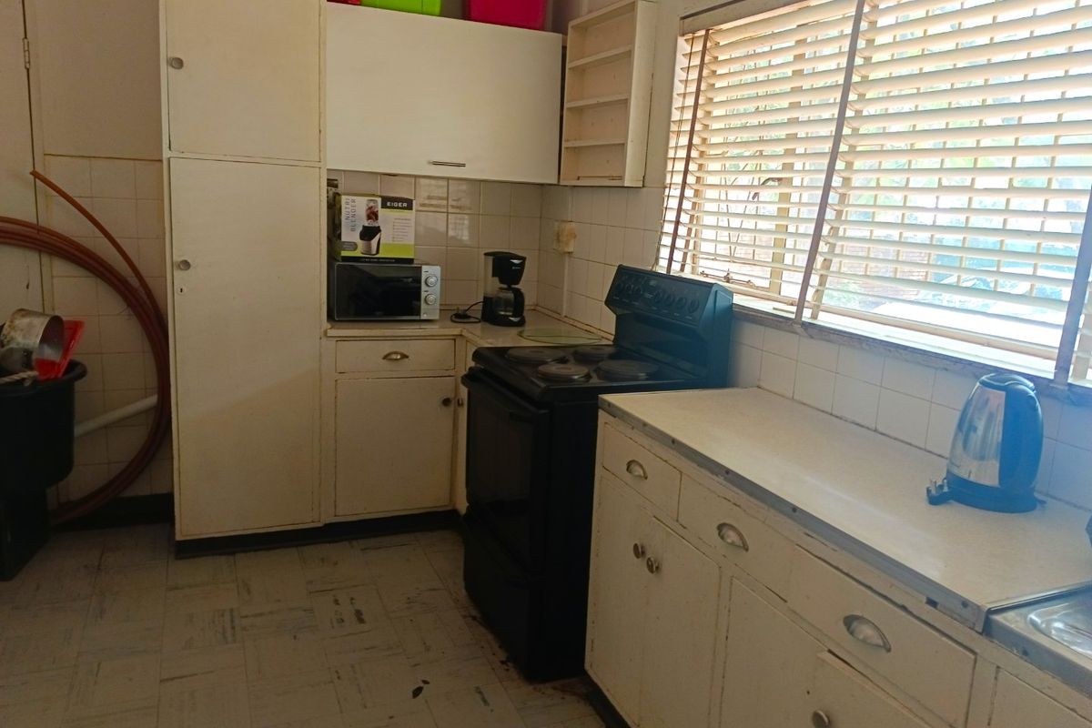 A dated kitchen featuring original cabinetry, tiled backsplash, and a freestanding stove, offering significant potential for modernization and renovation.