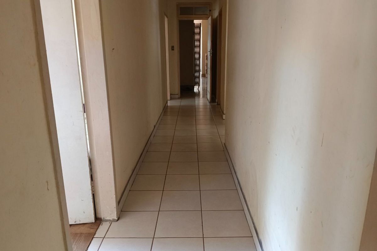 A vacant interior hallway featuring neutral ceramic floor tiles and multiple internal doorways, requiring cosmetic updates to the wall finishes.
