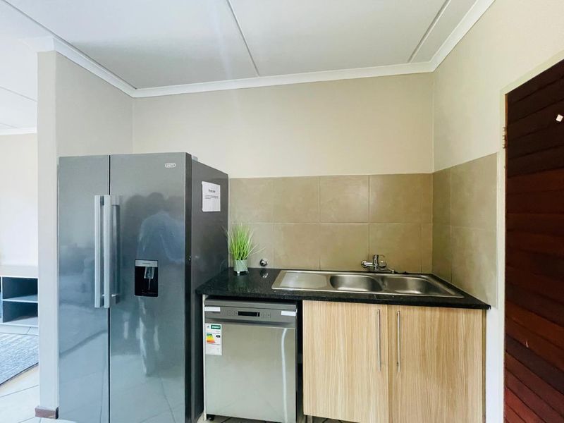 A functional scullery area featuring a double sink, granite countertops, tiled backsplash, and built-in wooden cabinetry.