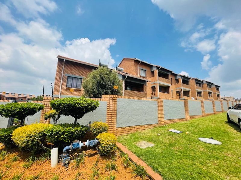 A view of the apartment complex exterior featuring a brick boundary wall, electric fencing, and landscaped garden area.