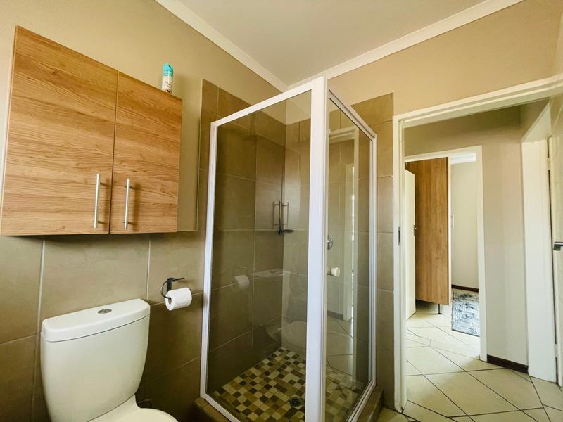 A functional bathroom featuring a shower enclosure, toilet, and wall-mounted cabinetry with neutral tiled finishes.