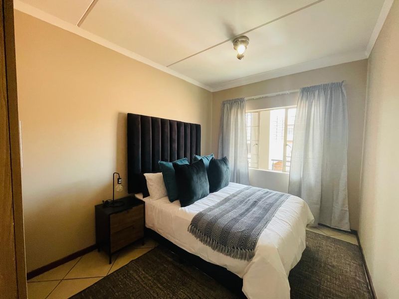 A well-lit bedroom featuring tiled flooring, a central ceiling light fixture, and a window with curtains.