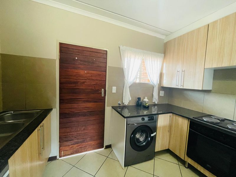A functional kitchen featuring light wood cabinetry, dark granite countertops, built-in oven and hob, and tiled flooring with direct access to an exterior door.