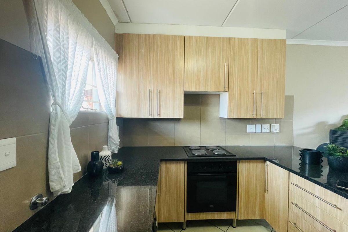 A functional kitchen featuring light wood-finish cabinetry, dark granite countertops, a built-in electric oven and hob, and neutral tiled backsplash.