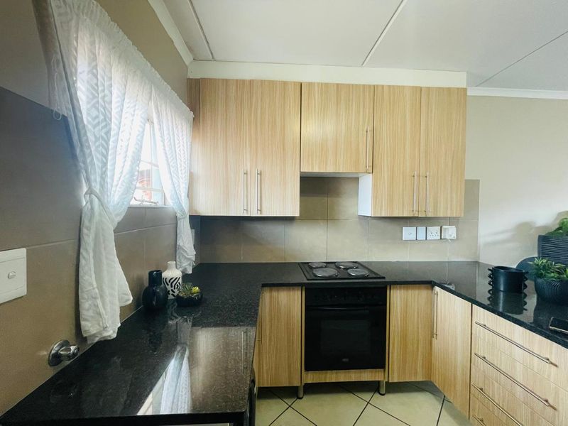 A functional kitchen featuring light wood-finish cabinetry, dark granite countertops, a built-in electric oven and hob, and neutral tiled backsplash.