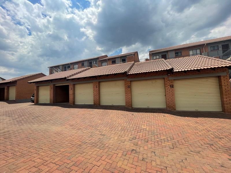 A row of secure, brick-built garages with roll-up doors and a paved driveway in a well-maintained apartment complex.