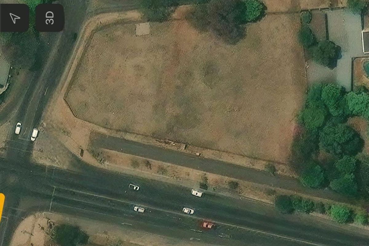 An aerial view of a vacant residential plot situated adjacent to a main road, offering clear access and potential for development.