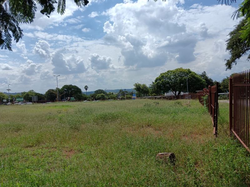 A vacant residential plot featuring open grassed land and perimeter metal fencing, offering a clear view of the surrounding neighborhood.