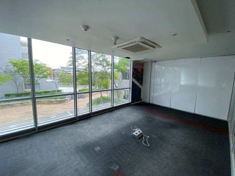 A vacant commercial office space featuring floor-to-ceiling windows, integrated ceiling air conditioning, and built-in storage cabinetry with views of the surrounding grounds.
