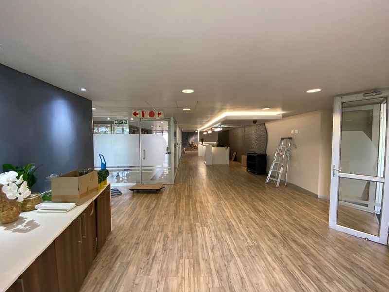 Spacious commercial entry area featuring wood-look flooring, recessed lighting, a glass partition, and a modern textured feature wall.