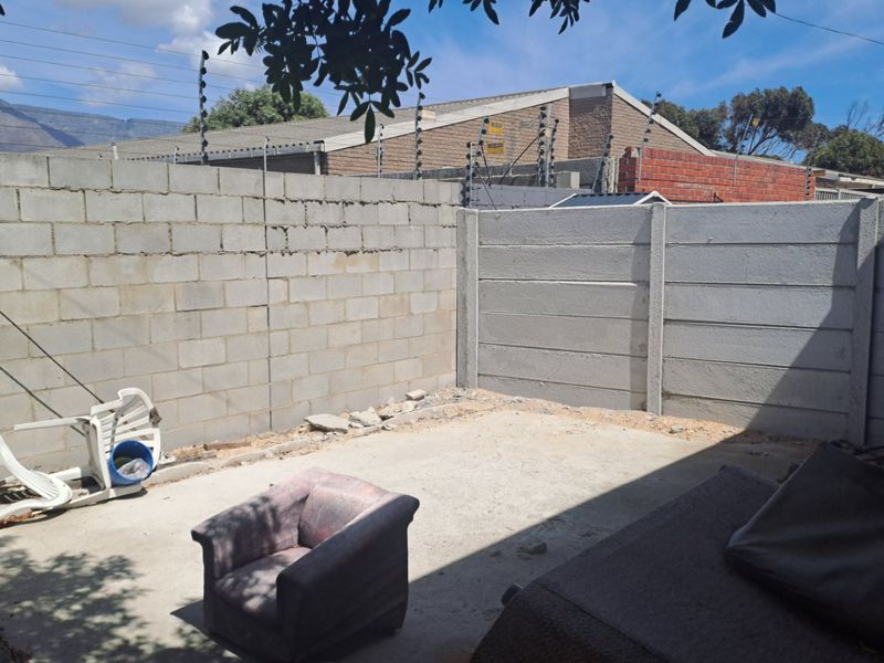 A rear outdoor area featuring a concrete patio slab enclosed by concrete block and precast boundary walls with installed electric fencing.