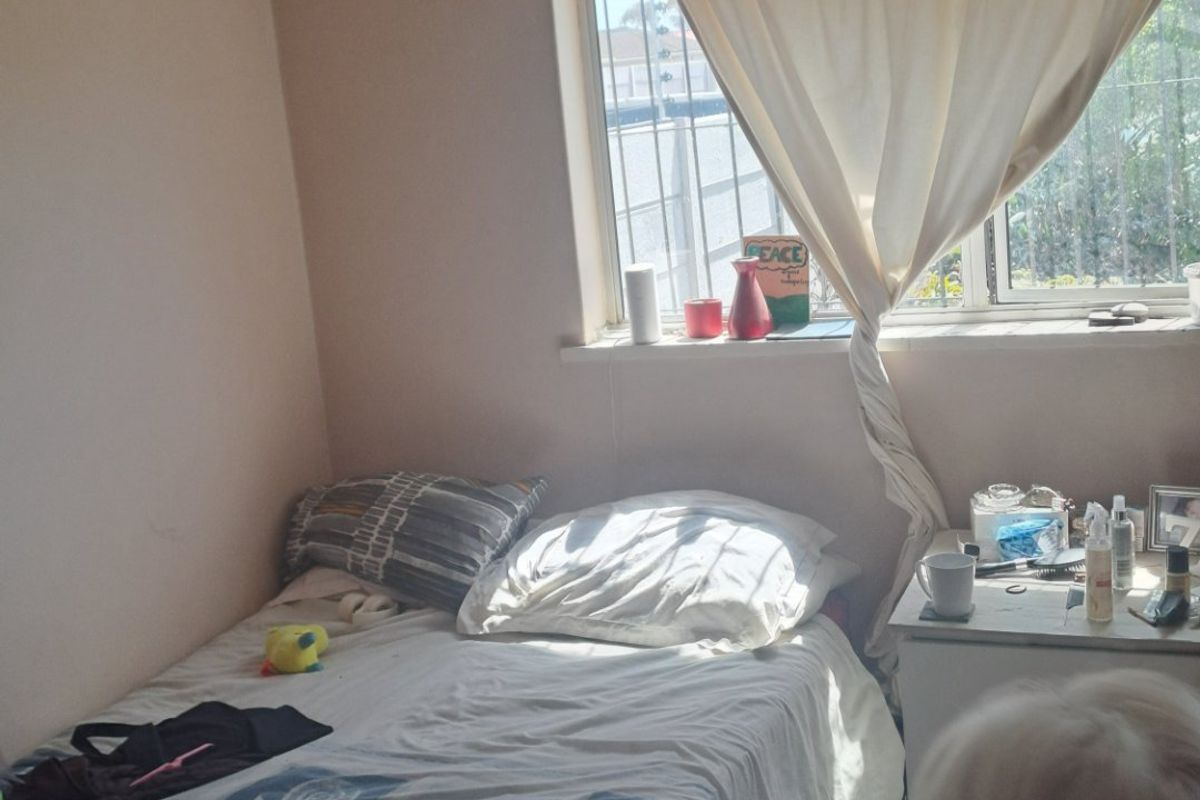 A bedroom featuring timber flooring and a window with a curtain rod, providing natural light.
