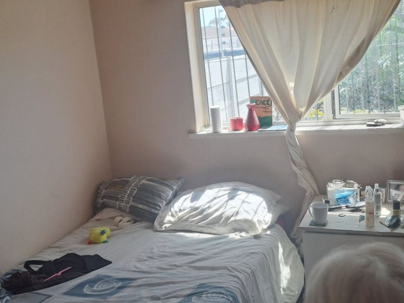 A bedroom featuring timber flooring and a window with a curtain rod, providing natural light.
