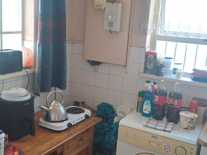 A compact kitchen area featuring wooden cabinetry, tiled splashbacks, and exposed electrical infrastructure, requiring cosmetic updates to improve functionality and aesthetic appeal.