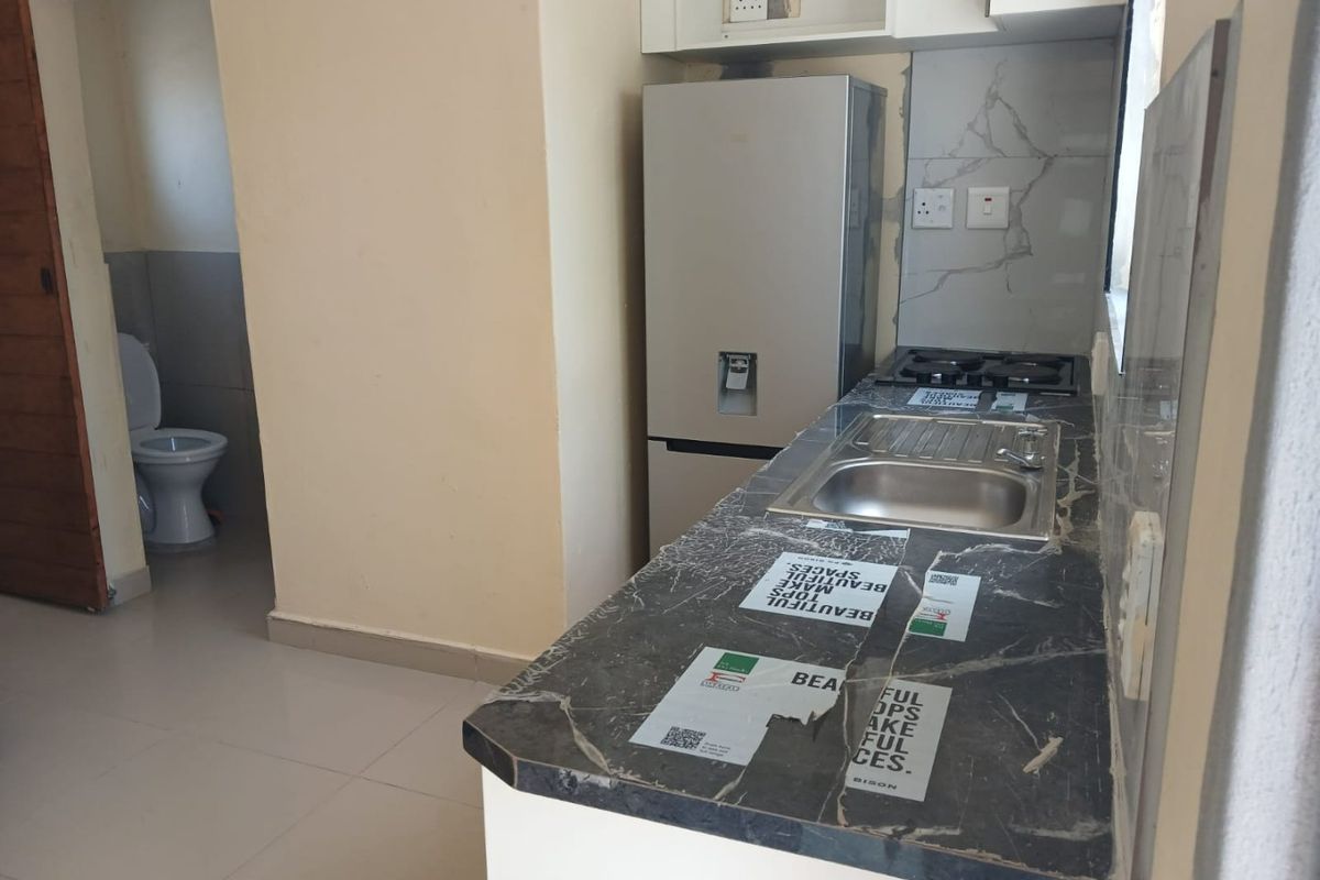 Compact kitchen featuring marble-effect countertops, a gas hob, and stainless steel sink, with adjacent access to a bathroom area.