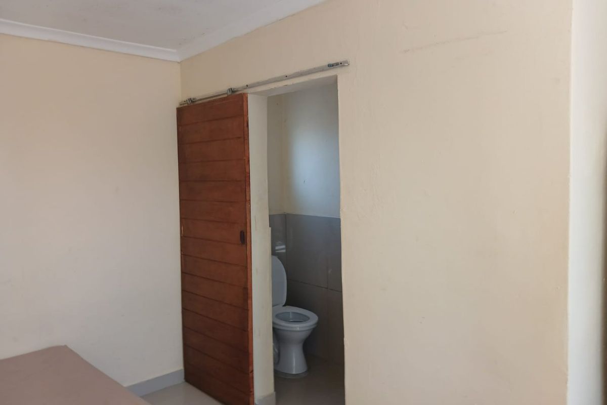 A bedroom featuring a sliding wooden door leading to an en-suite toilet, with plain walls and basic finishes.