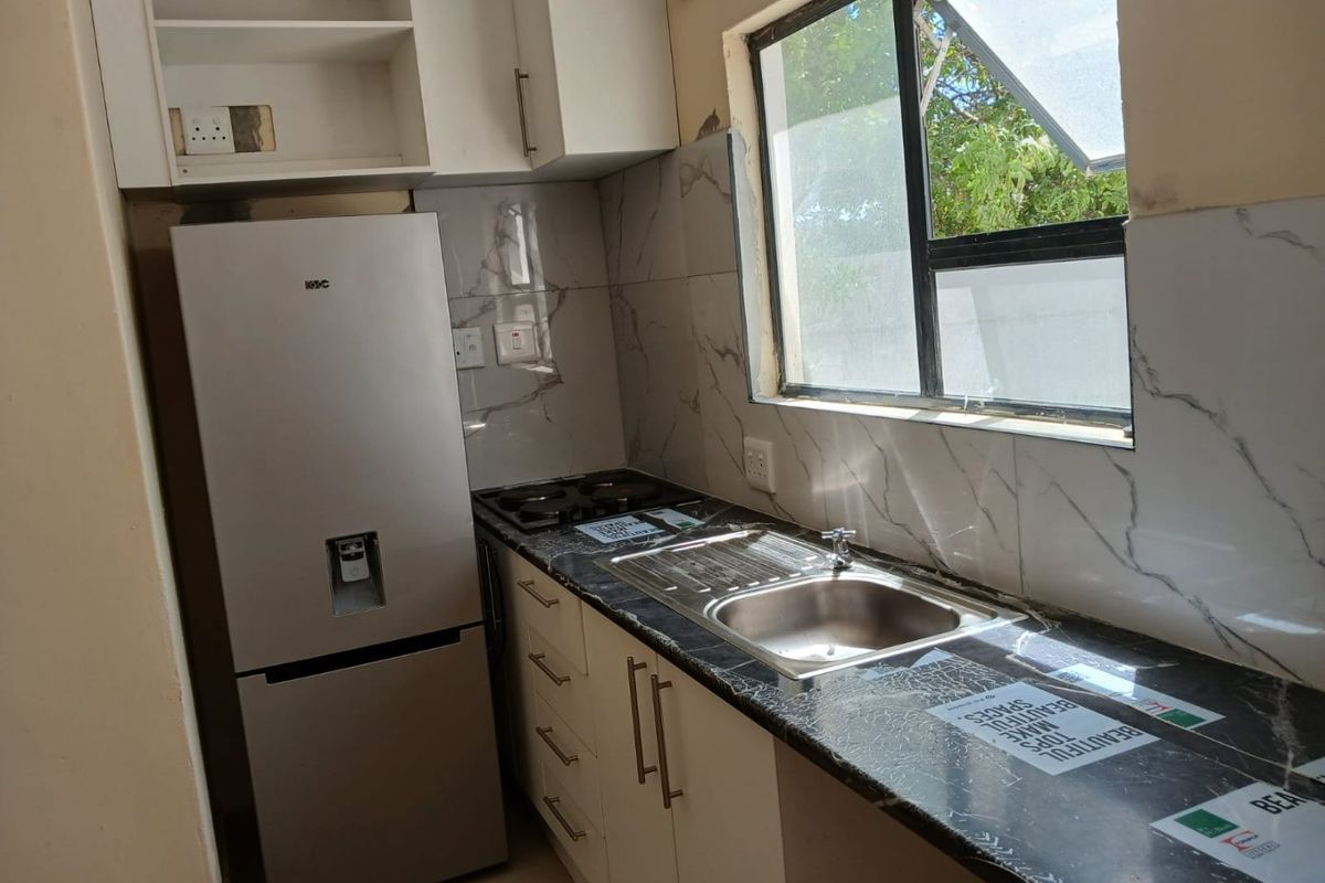 Compact kitchen featuring marble-effect countertops, tiled splashbacks, built-in gas hob, and stainless steel sink with modern cabinetry.