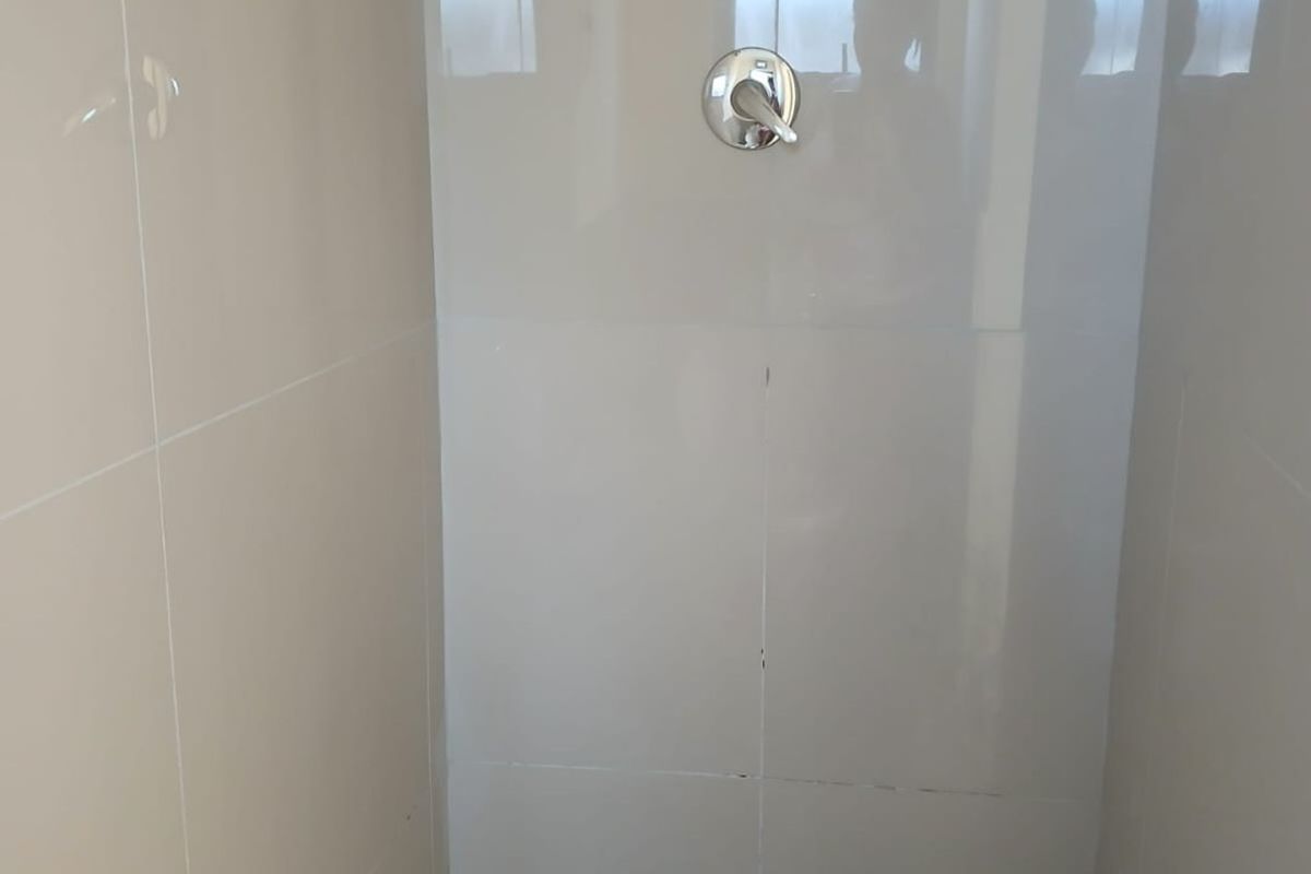 A clean, modern shower enclosure featuring neutral wall tiles, a mosaic-tiled floor, and a chrome mixer tap.