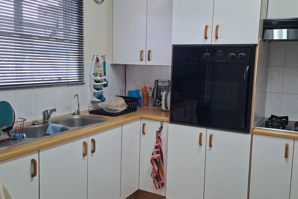 Functional kitchen featuring white cabinetry, laminate countertops, a double stainless steel sink, built-in oven, gas hob, and an extractor fan.