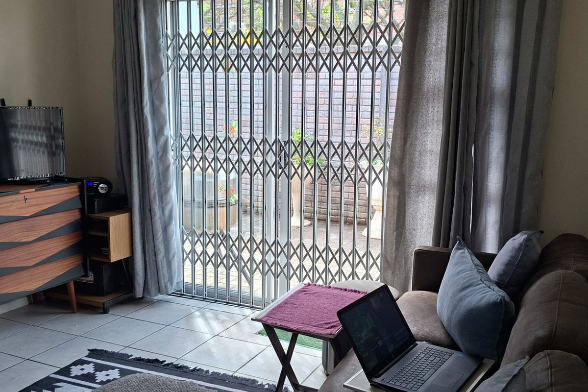 A living room featuring tiled flooring and a sliding glass door with a security gate leading to an outdoor area.