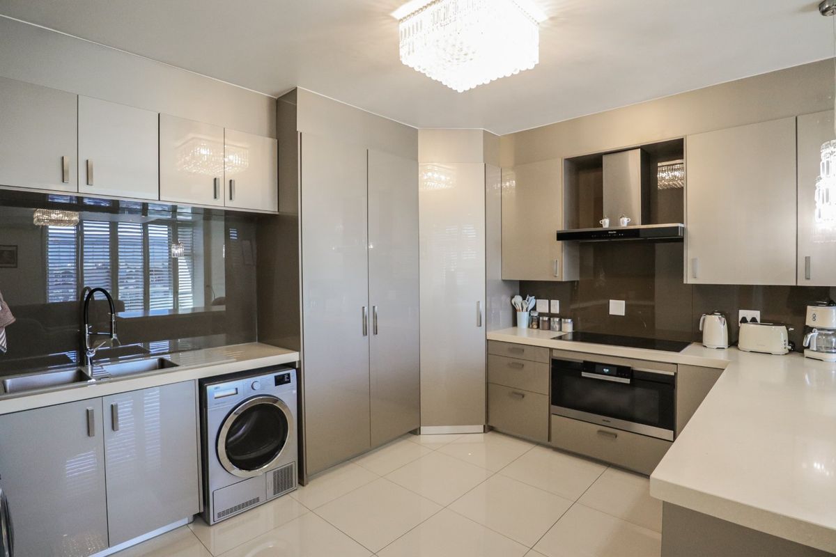 Modern kitchen featuring high-gloss cabinetry, stone countertops, integrated appliances, induction hob, and sleek glass splashbacks with polished tiled flooring.