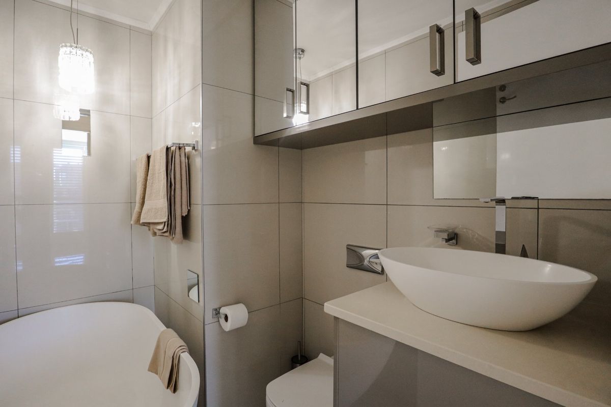 Modern bathroom featuring a sleek vessel sink, vanity cabinet with mirrored storage, and a freestanding bathtub with contemporary wall-mounted fixtures.