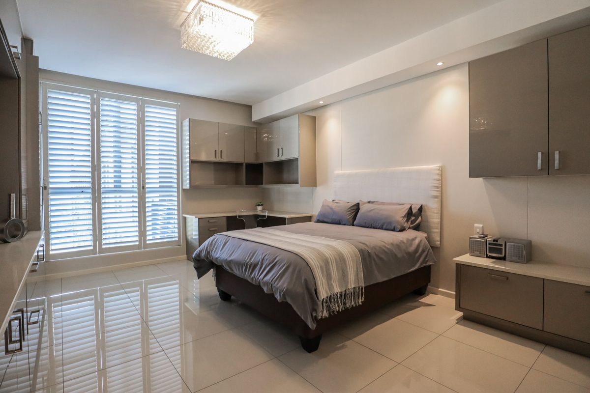 Modern bedroom featuring high-gloss built-in cabinetry, integrated desk space, polished tile flooring, and elegant shutter blinds for natural light control.