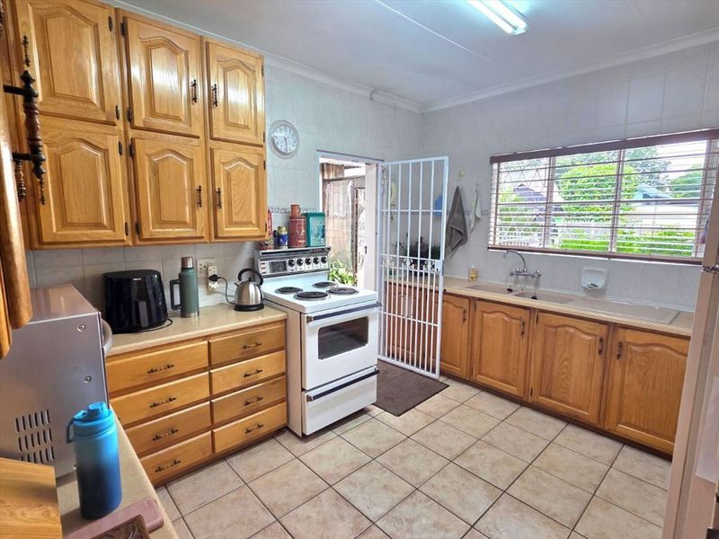 A functional kitchen featuring traditional wooden cabinetry, tiled flooring, a freestanding stove, and a double basin sink with natural light.