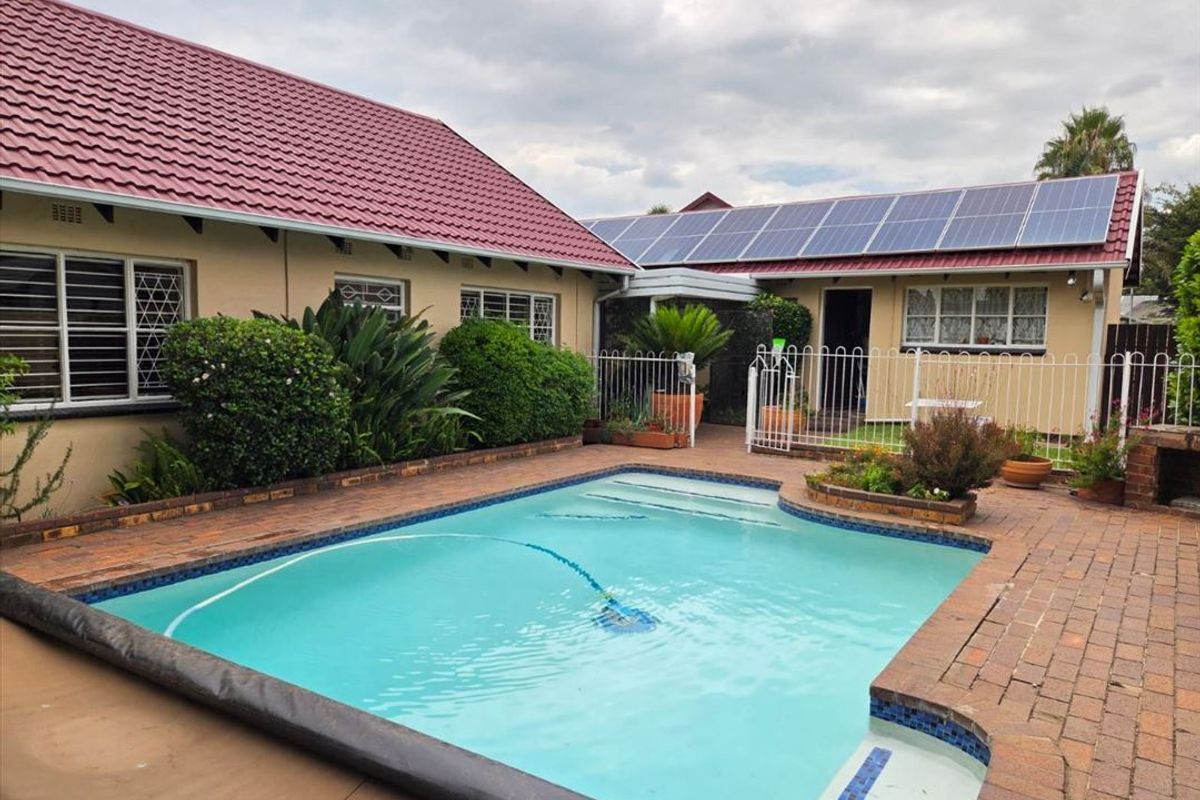 A well-maintained outdoor pool area featuring brick paving, metal fencing, and a roof equipped with solar panels.