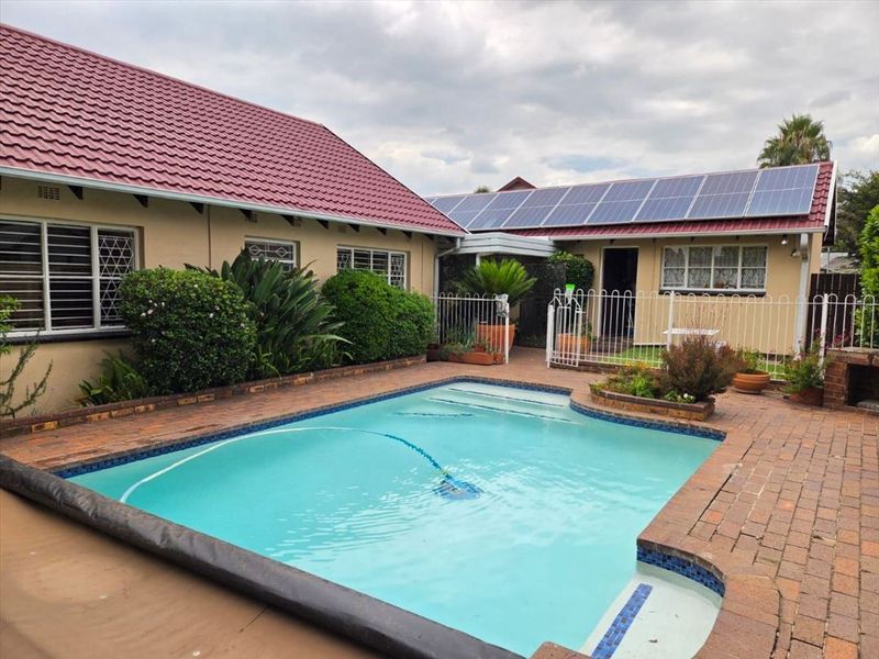 A well-maintained outdoor pool area featuring brick paving, metal fencing, and a roof equipped with solar panels.