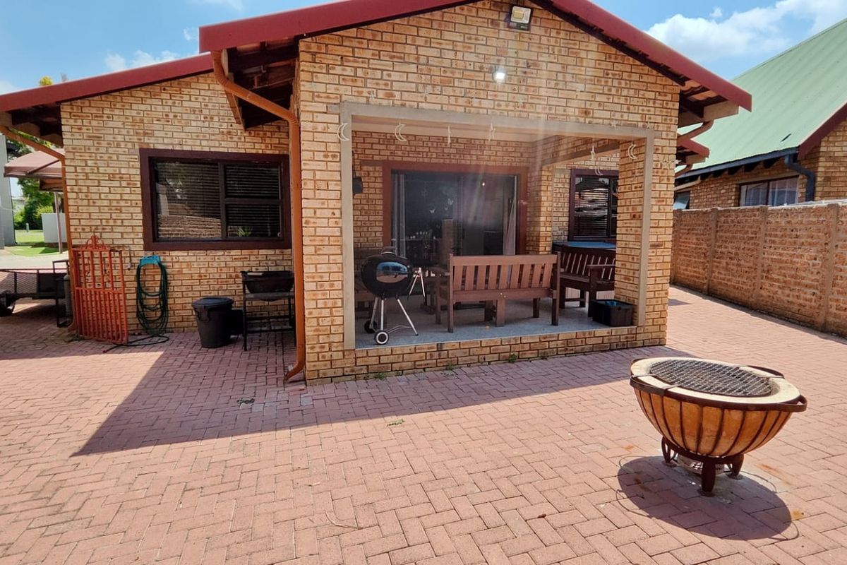 Rear view of a face brick house featuring a covered patio area and a spacious paved courtyard, ideal for outdoor entertaining.
