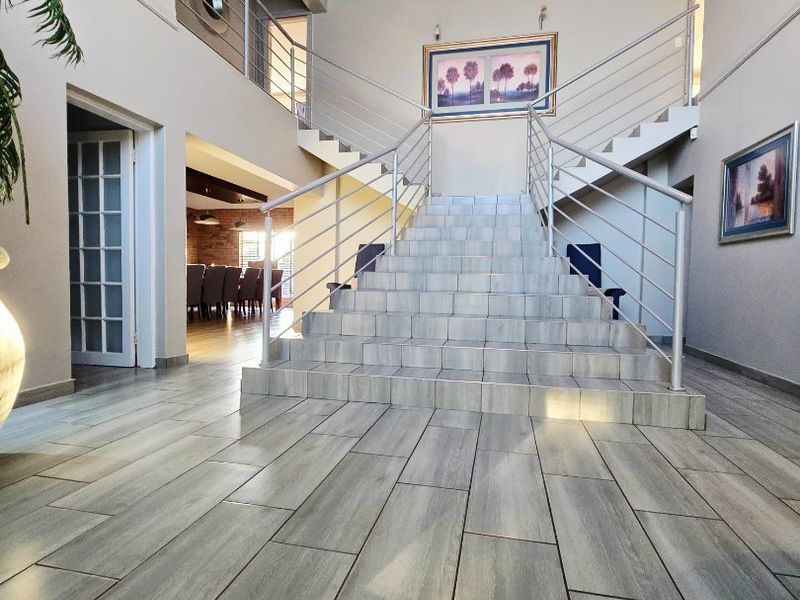 Grand entrance hall featuring a central tiled staircase with stainless steel balustrades, double volume ceilings, and access to the dining area.