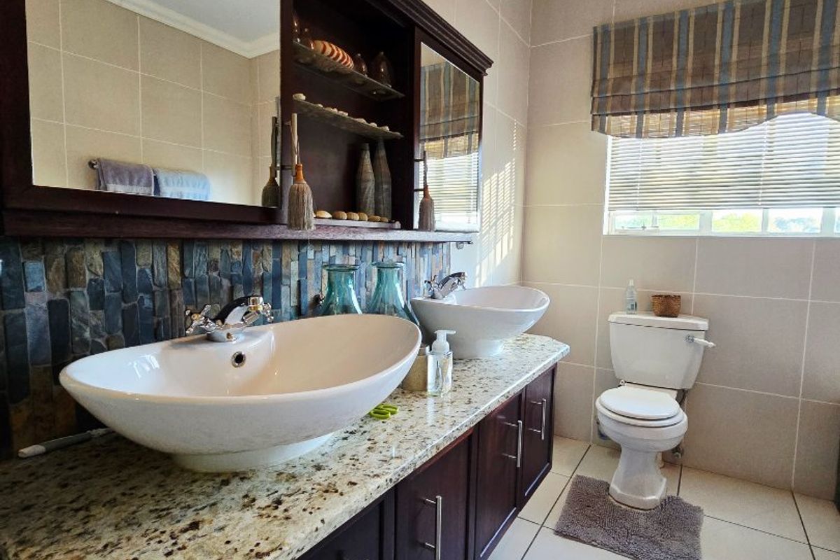 A well-maintained bathroom featuring a double vanity with granite countertops, vessel sinks, and a built-in mirror cabinet with stone tile backsplash.