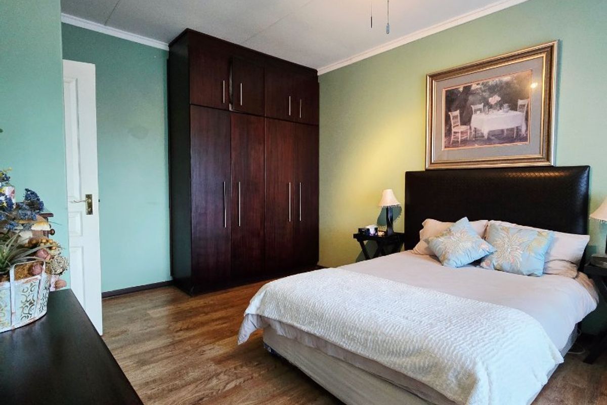 A well-maintained bedroom featuring laminate flooring, built-in dark wood cupboards, and a ceiling fan.